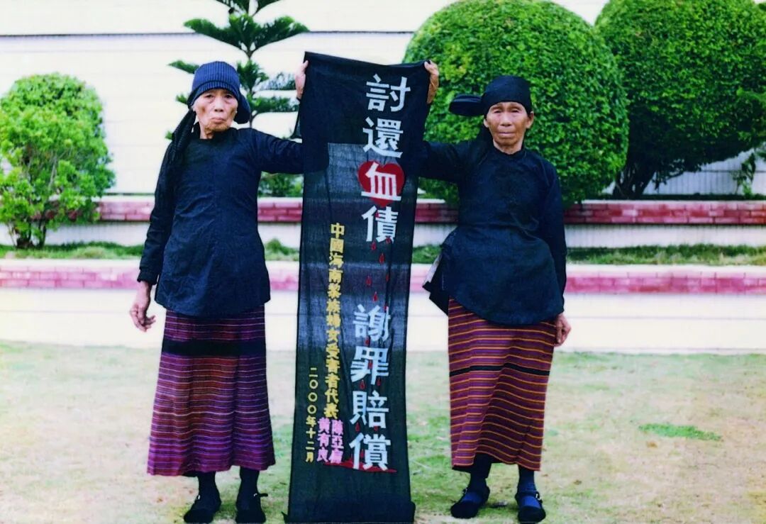 2000年12月，海南最早站出来起诉日本政府的黄有良(右)和陈亚扁穿着民族服装，在日本东京打出她们亲手绣有“讨还血债,谢罪赔偿”的织品,控诉侵华日军的罪行。图/李晓方提供